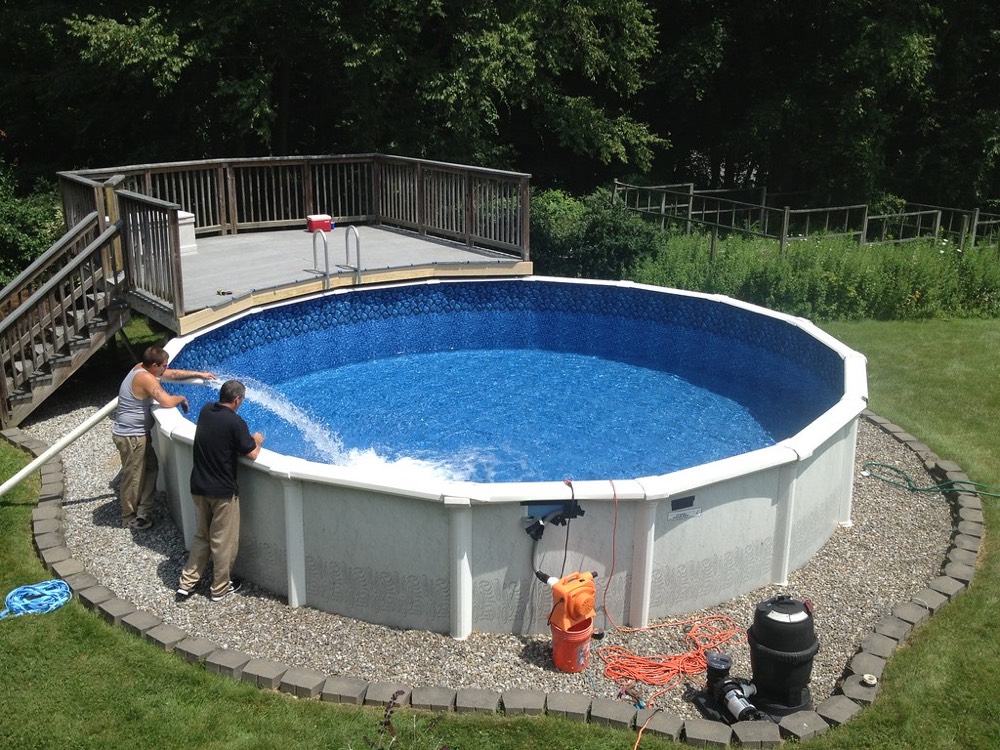 Dos personas llenando de agua una piscina desmontable redonda de armazón en un jardín